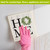 Home Swedish Dishcloth, pink glove hand holding white dishcloth with green wreath and home sign.