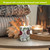 Patterned Ornaments Flameless Candle, white with green pine and plaid ornament designs, lit on table.