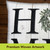 White indoor pillow with large black H's and green leaves on a wooden background decorative throw.