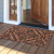Black Damask coir doormat, 24 x 36, on wooden porch in front of open door.
