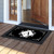 Black and white monogram doormat with decorative floral design and letter A on wooden porch floor.