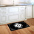 Black and white monogram doormat with floral design on wooden floor beside white kitchen cabinets.