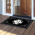 Black and white monogram doormat with decorative floral design and large "M" on wooden porch floor.