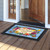 Bless This Home With Love doormat with floral design on wooden porch in front of doorway.