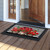 Black doormat with white stripes and red geraniums on a wooden porch outside an open doorway.
