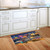 Oceanside Fireworks Doormat on wooden floor in front of white kitchen cabinets and sink area.