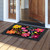 Vibrant floral doormat with colorful flowers on a black background outside a doorway on wooden floor.