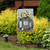 Garden flag with floral design, black and white checkered background, and vase with orange daisies.