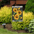 Elegant garden flag with vibrant yellow sunflowers and green leaves on a black background with white flowers.
