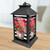 Black metal lantern with red geraniums and striped pattern on a wooden surface.