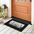 Black doormat with checkered mason jars and purple flowers design on front porch with brown door.