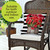 Brown wicker chair with white cushion and striped pillow, holding red flowers in a wooden planter.