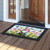Springtime gnome doormat with colorful floral design and butterfly, on a wooden porch floor.