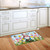 Springtime gnome doormat on wooden floor in front of white kitchen cabinets with colorful floral design.