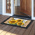 Sunflower Duo Doormat with yellow sunflowers and checkered pattern on a wooden porch outside doorway.
