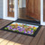 Spring Bunny Trio Doormat with colorful floral design and bunnies on a wooden porch outside doorway.