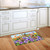 Spring Bunny Trio Doormat on wooden kitchen floor with colorful floral design and three bunnies.