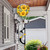 Checkered sunflowers hot air balloon spinner on pole outside house with garden and garage background.