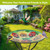 Ladybugs and Sunflowers glass birdbath with metal stand displayed outdoors in a garden setting.