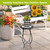 Black metal Home Plant Stand holding potted plant on decorative tile patio with garden bench.
