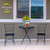 Briarwood Lane Floral Birdhouses Medium Planter with yellow flowers on outdoor table between two black chairs.