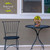 American Barn Star small metal planter with yellow flowers on a black patio table and chair.