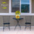 Sunflower Dance Medium Planter with yellow flowers on a small black outdoor table between two chairs.