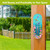Dragonfly Garden Metal Thermometer with colorful flowers and dragonflies on a wooden post outdoors.