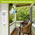 White Home Metal Thermometer mounted on wall beside porch with wicker chairs and greenery outside.