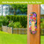 Zinnias in Bloom metal thermometer with colorful floral design on a wooden post outdoors.