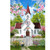 White church with red roof and steeple surrounded by flowers and picket fence in spring.
