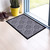 Large gray paisley doormat with black border on light wood floor beside door and potted plant.