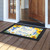 Bless This Home floral doormat with sunflowers and blue text on a black background outside doorway.
