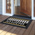 Black and white checkerboard doormat with gold accents and welcome text on wooden porch floor.