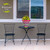Medium Neon Checkerboard Planter with yellow flowers on a small black outdoor table between two chairs.