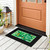 Black mini doormat with green Happy St. Patrick's Day design on a porch.
