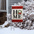 Holiday Home Burlap Garden Flag with red plaid border and festive wreath on snowy display.