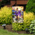 Easter Sunrise Cross Garden Flag with purple cloth and white flowers on a garden stand outdoors.
