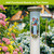 Spring Celebration Birdhouses Metal Thermometer mounted on a post amidst flowers and greenery outdoors.