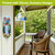 Spring Celebration Birdhouses Metal Thermometer on a porch wall with colorful garden decorations nearby.