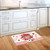 Red and pink heart patterned Love Bouquet Doormat on wooden kitchen floor beside white cabinets.