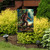Believe Bigfoot garden flag with colorful Sasquatch design and text on a black metal stand outdoors.