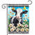 Black and white cow surrounded by white daisies and butterflies on checkered garden flag.
