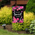 Home Sweet Home garden flag with pink flowers and hummingbirds on a black background outdoors.