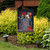 American Watering Can Garden Flag with patriotic design and floral pattern on a garden stand outdoors.