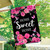 Black garden flag with pink roses, hummingbirds, and "Home Sweet Home" text on a wooden pole.