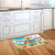 Beach themed doormat on wooden floor in front of white kitchen sink and cabinets.