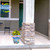 Multicolored With God Medium Planter with yellow flowers on a house porch next to a pillar.