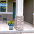 Blue and gold medium planter with yellow flowers on a house porch with stone pillar nearby.