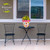 Vibrant Blooms medium planter with yellow flowers on a black table between two black metal chairs.